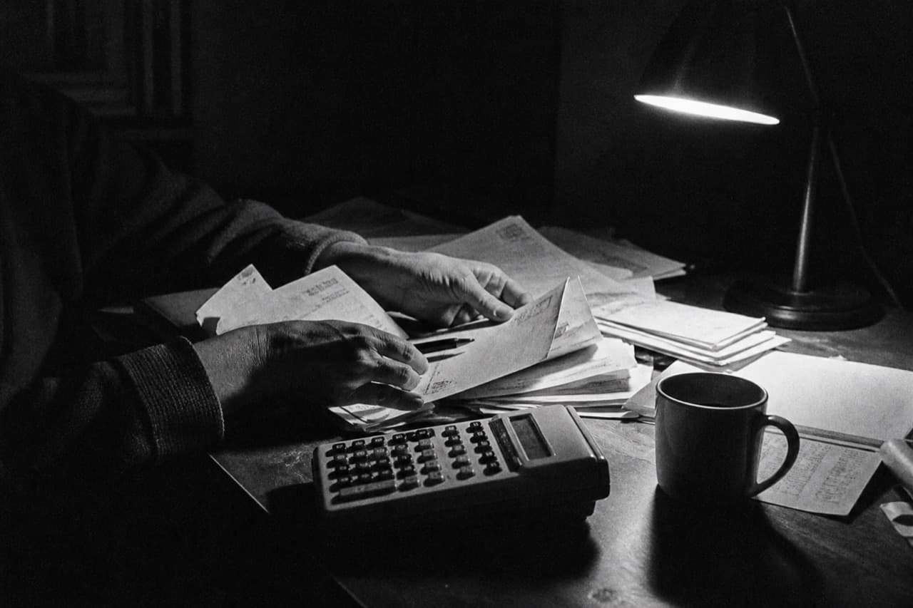 Hands sorting bills under a desk lamp at night