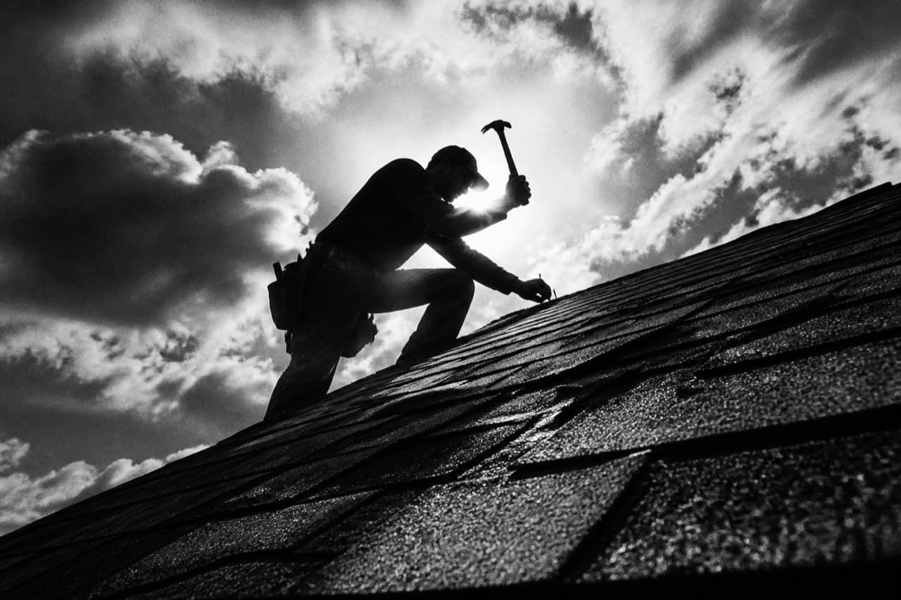 Roofer silhouetted on a shingle roof against the sky