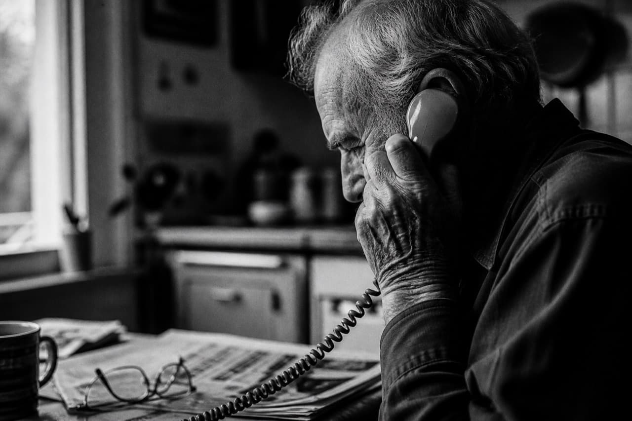Elderly man taking a phone call at his kitchen table
